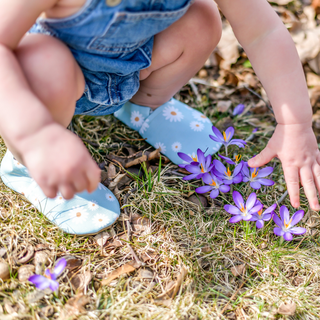 Child wearing Custom Cabooties baby shoes kneels outside among flowers