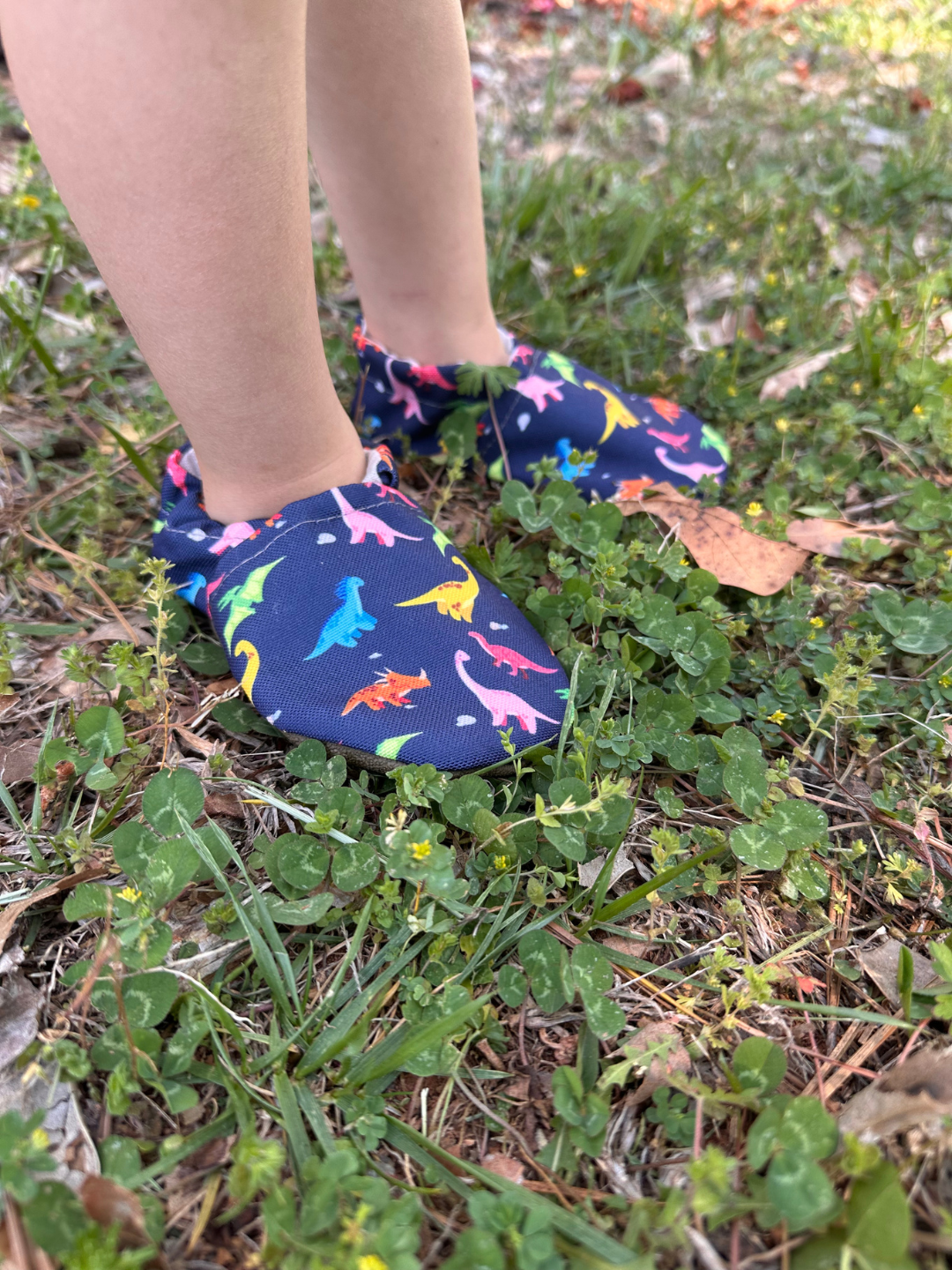 Lifestyle photo - toddler wearing Rainbow Dino Cabooties Baby Shoes outside in grass