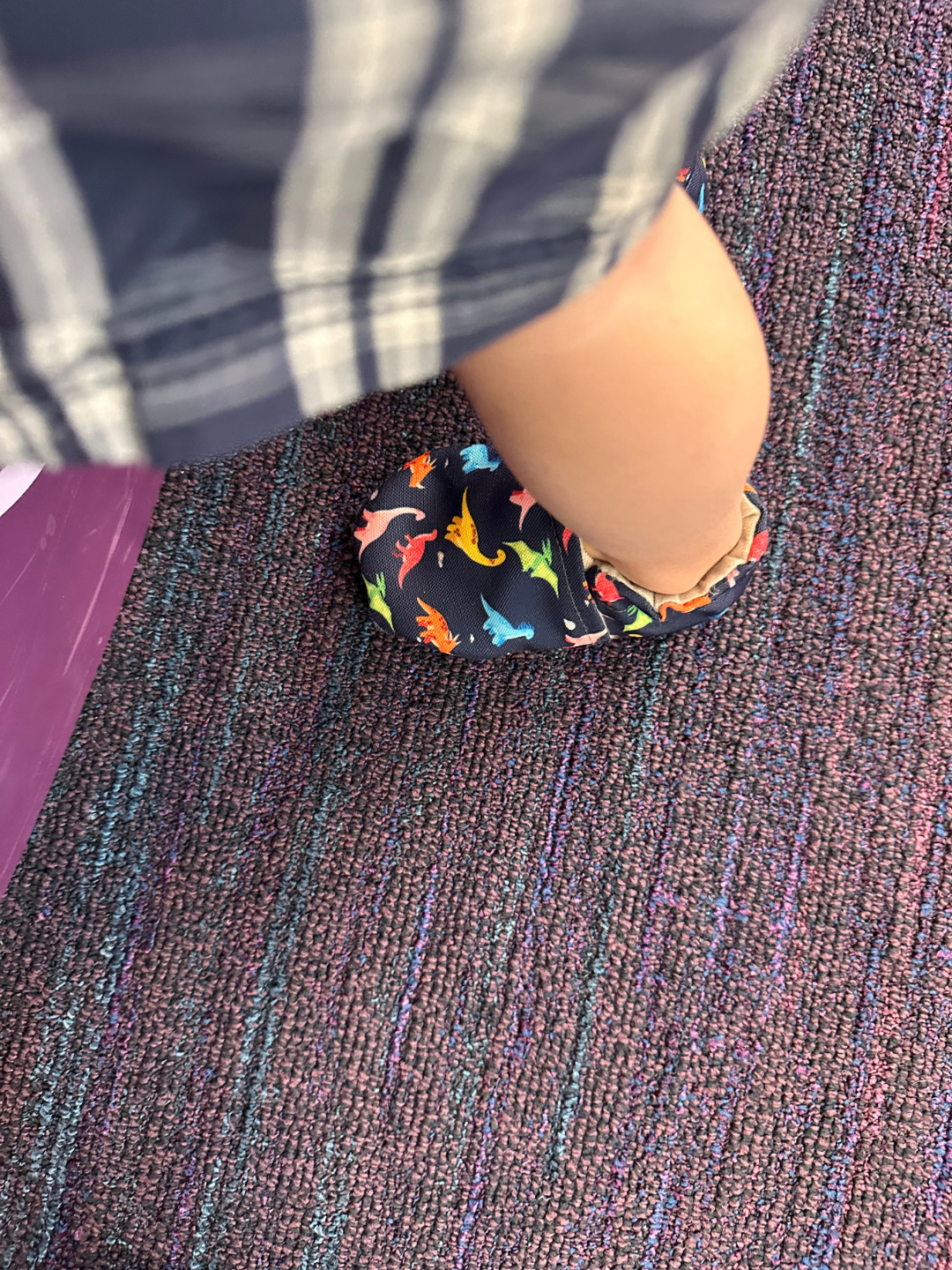 Lifestyle photo - toddler wearing Rainbow Dino Cabooties Baby Shoes at a kids play museum on purple carpet