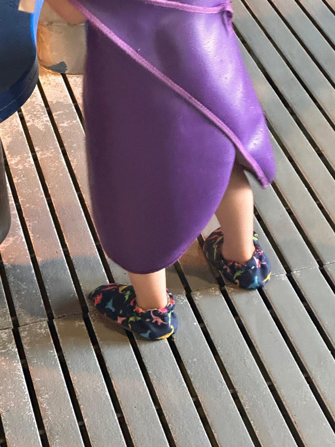 Lifestyle photo - toddler wearing Rainbow Dino Cabooties Baby Shoes at Port Discovery Kids Museum in Baltimore - child is in protective splash suit for the indoor water play exhibit